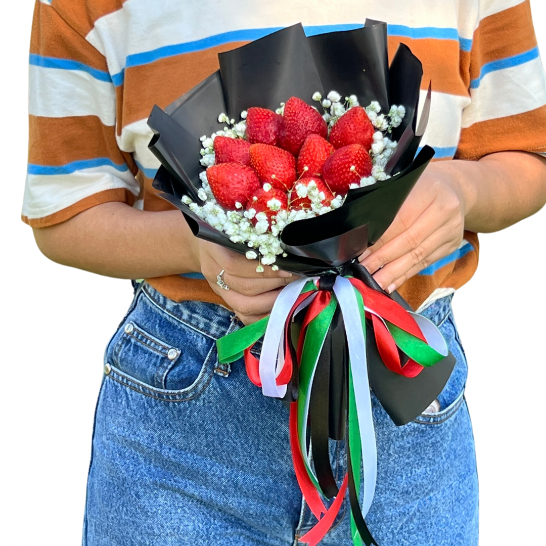 Person holding a bouquet of strawberries with decorative ribbons on a white background