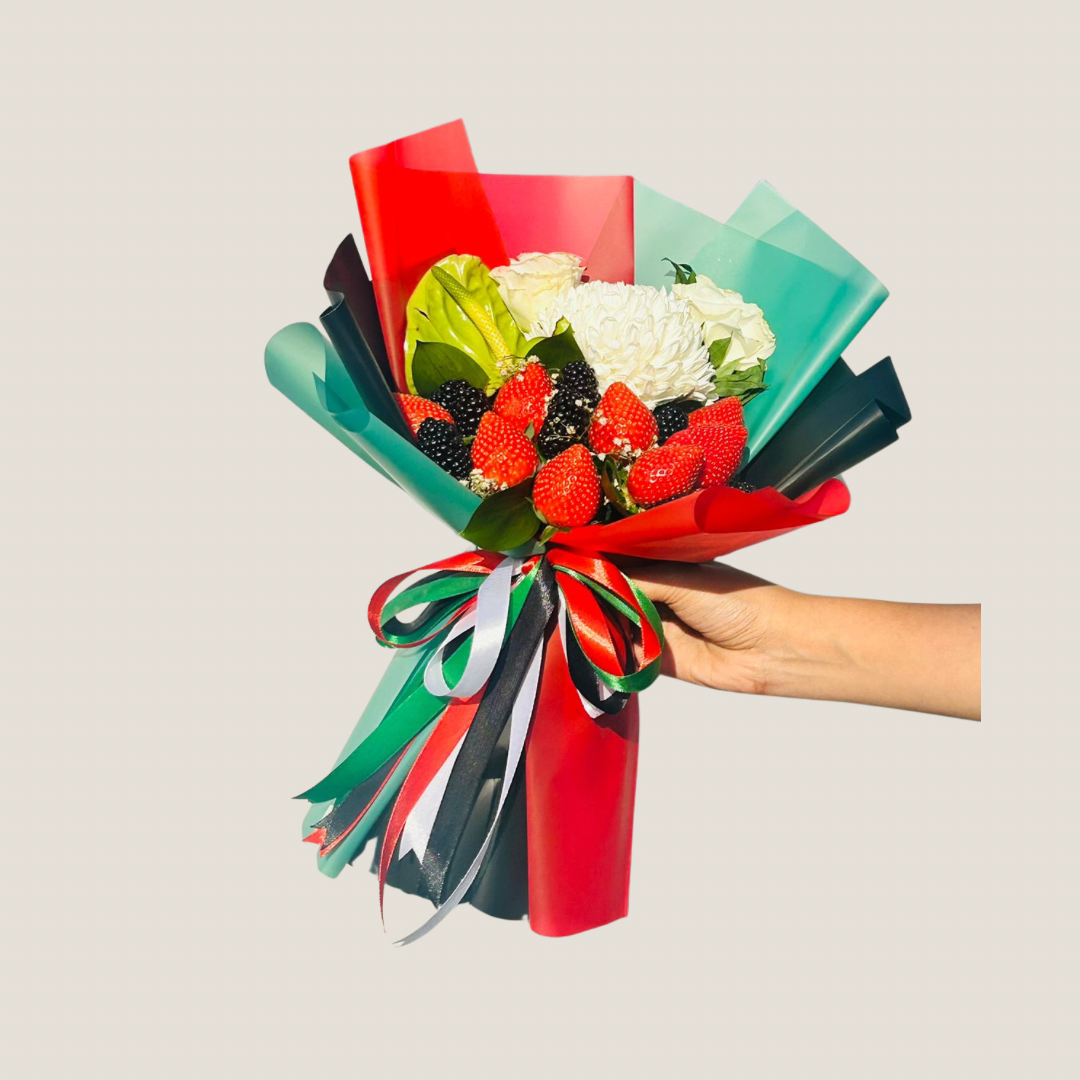 Bouquet of flowers with red and green ribbons held by a hand on a light gray background