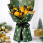 Bouquet of fruits wrapped in green paper with gold tree patterns, surrounded by Christmas decorations.