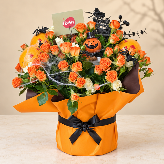 A Halloween-themed rose bouquet wrapped in bright orange paper with a black ribbon bow, filled with orange and white roses, small pumpkins, spider decorations, black branches, and a small sign that reads 'Frufty'.