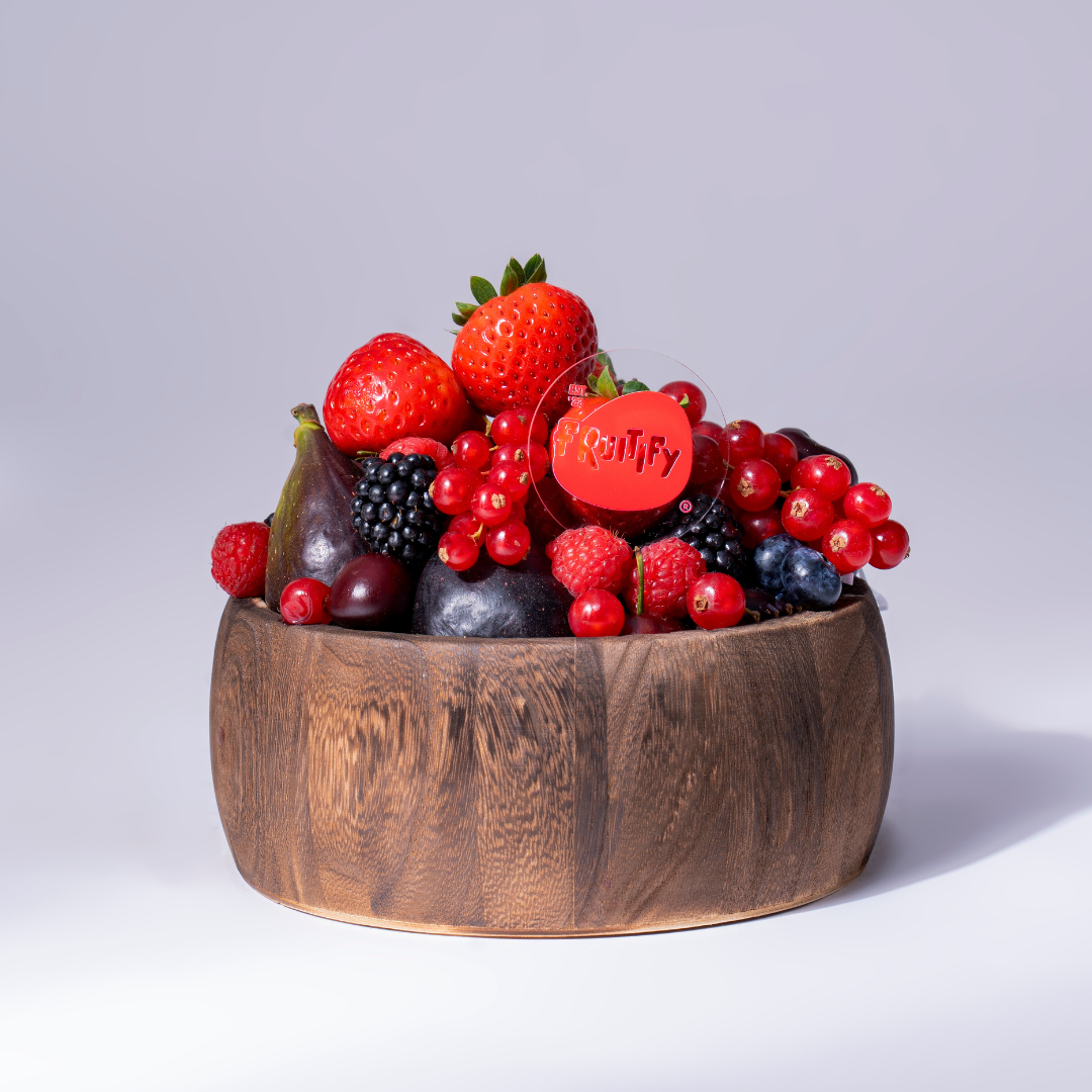 Wooden bowl filled with a variety of fruits on a light gray background