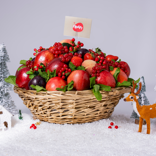 Fruit basket with apples, berries, and a 'Fruitfly' sign on a snowy background with Christmas decorations.