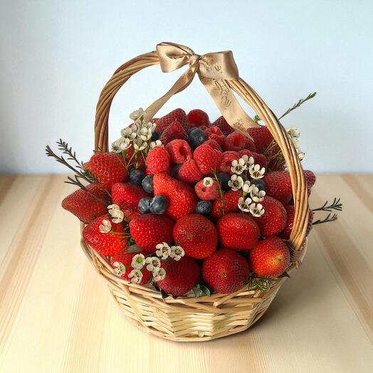 Basket of strawberries with a gold bow on a light wooden surface
