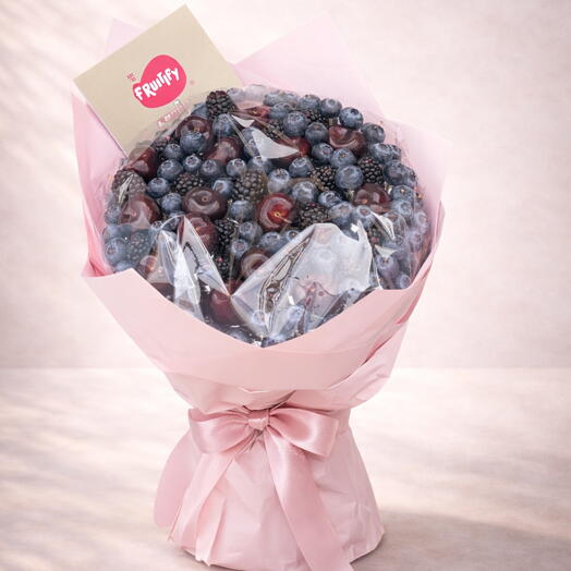 Bouquet of assorted berries wrapped in pink paper with a bow on a light pink background