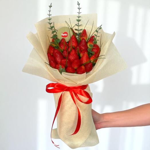 Bouquet of strawberries wrapped in brown paper with a red ribbon, held against a white background.