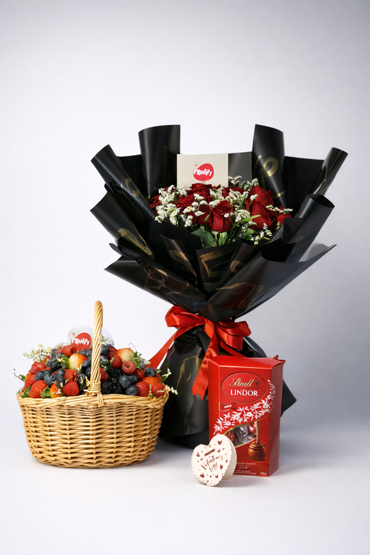 Bouquet of flowers wrapped in black paper with a box of Lindt chocolate, fruit basket, and heart-shaped object on a light gray background.