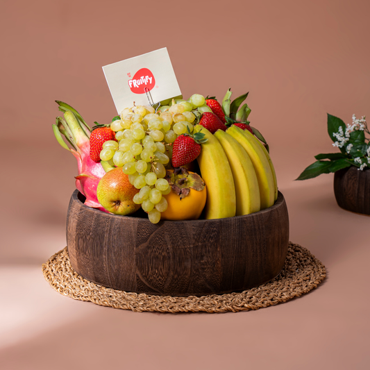 Fruit basket with bananas, grapes, and strawberries in a wooden bowl on a brown background