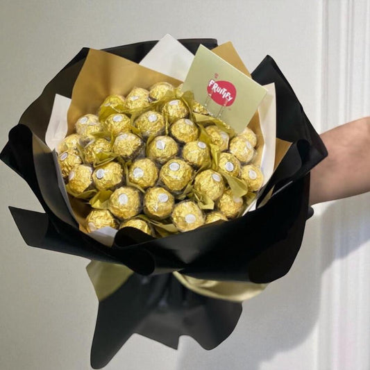 Bouquet of Ferrero Rocher chocolates wrapped in gold paper and black ribbon, held by a person.