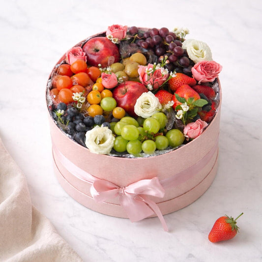 Fruit and flower arrangement in a pink box on a white background