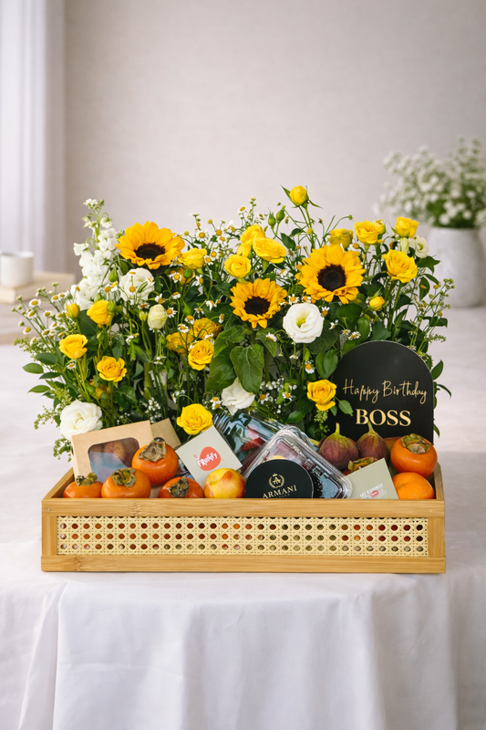 Gift basket with flowers, fruits, and a card on a white tablecloth.