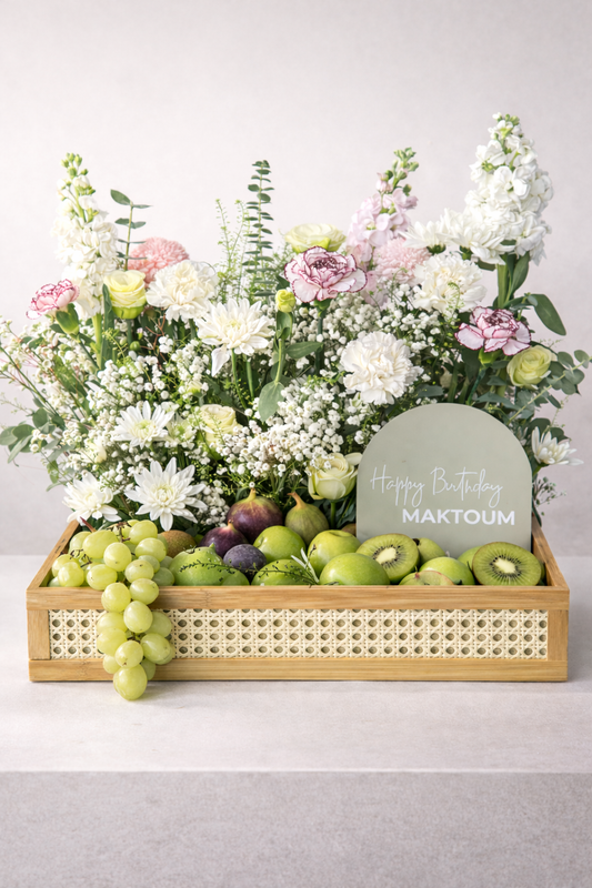 Fruit and flower arrangement with a personalized card on a light gray background