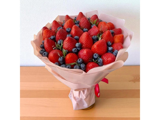 Bouquet of strawberries and blueberries wrapped in brown paper on a wooden surface.
