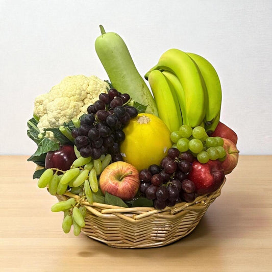 Basket of fruits and vegetables including bananas, apples, grapes, and a cauliflower on a wooden surface.