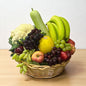 Basket of fruits and vegetables including bananas, apples, grapes, and a cauliflower on a wooden surface.