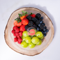 Assorted berries including strawberries, raspberries, blackberries, and blueberries on a wooden platter with 'Fruity' branding.