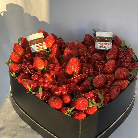 Heart-shaped arrangement of strawberries and red currants with Nutella jars on a gray background
