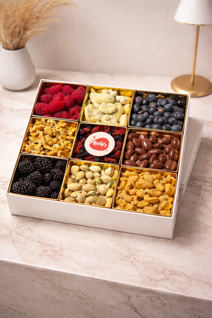 Assorted dried fruits and nuts in a white box on a marble surface.