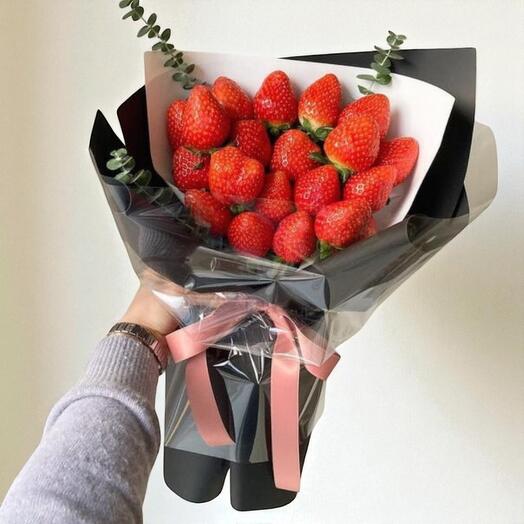 Bouquet of strawberries wrapped in black paper with a pink ribbon, held by a person.