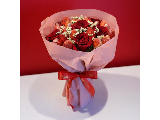 Bouquet of red roses and strawberries wrapped in pink paper with a red ribbon on a white surface.