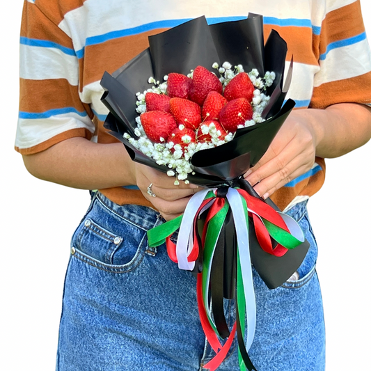 Person holding a bouquet of strawberries with decorative ribbons on a white background
