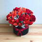 Bouquet of strawberries and red roses in a black box with a red ribbon on a wooden surface.