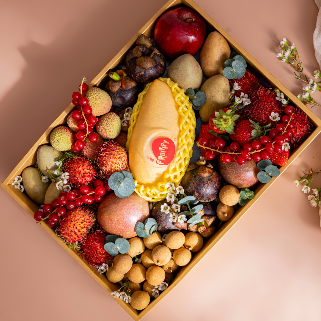 Assorted fruits and a yellow soap bar with a heart label in a decorative box on a pink background.