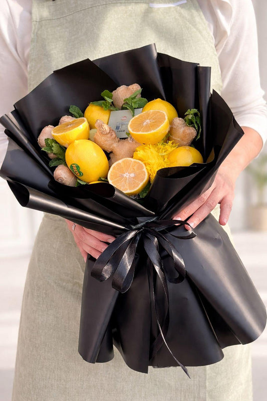 Bouquet of lemons and chicken wrapped in black paper held by a person.