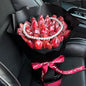 Bouquet of red strawberries with a pearl necklace wrapped in black paper and a red ribbon inside a car.